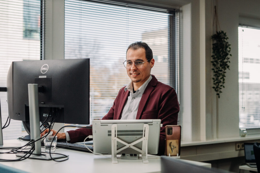 Man werkt staand achter een bureau met computer in een modern kantoor.