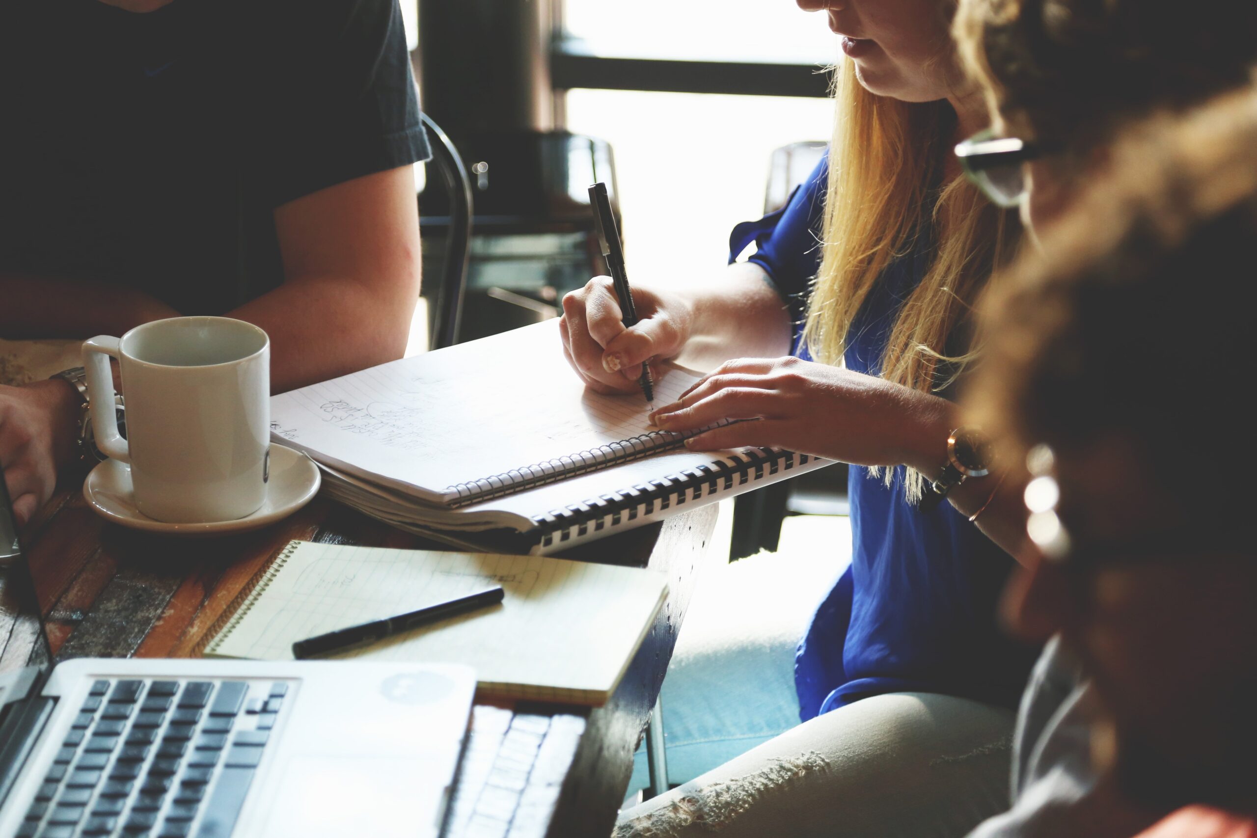 Teamleden werken samen aan tafel met notitieboek en laptop